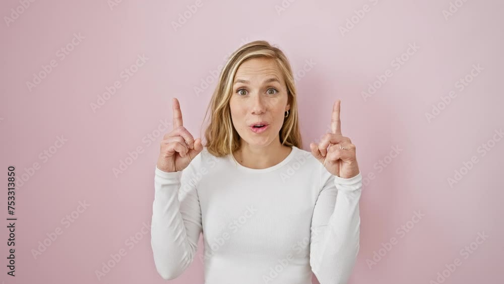 Young, beautiful blonde woman overjoyed with girlish joy - pointing upwards with a look of surprise on her face, standing against a whimsical isolated pink backdrop. Young, beautiful blonde woman overjoyed with girlish joy - pointing upwards with a look of surprise on her face, standing against a whimsical isolated pink backdrop.