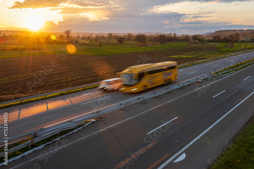 Yellow bus drive at high speed on the highway through the rural landscape. Fast blurred highway driving. A scene of speeding on the highway. Beautiful sunset in the background. Beautiful sunset in the