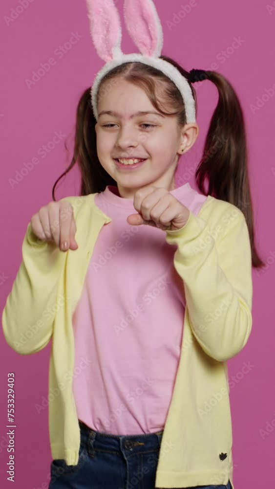 Vertical Video Joyful carefree schoolgirl jumping around in studio, imitating a rabbit and hopping against pink background. Cheerful active child wearing bunny ears and bouncing, adorable kid. Camera Vertical Video Joyful carefree schoolgirl jumping around in studio, imitating a rabbit and hopping against pink background. Cheerful active child wearing bunny ears and bouncing, adorable kid. Camera