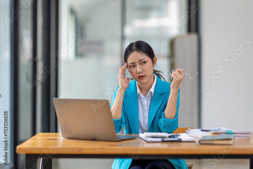 Portrait of tired young business Asian woman work with documents tax laptop computer in office. Sad, unhappy, Worried, Depression, or employee life stress concept	