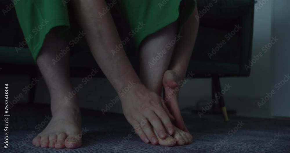 Massaging his foot, man tries to relieve pain in his legs. Man kneads and massages his foot, close-up. Mature man with arthritis is sitting on the bed, rubbing his ankle and foot to alleviate pain