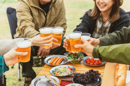 秋冬のキャンプ場で仲間と一緒にビールを飲んでパーティーする男女の手元 