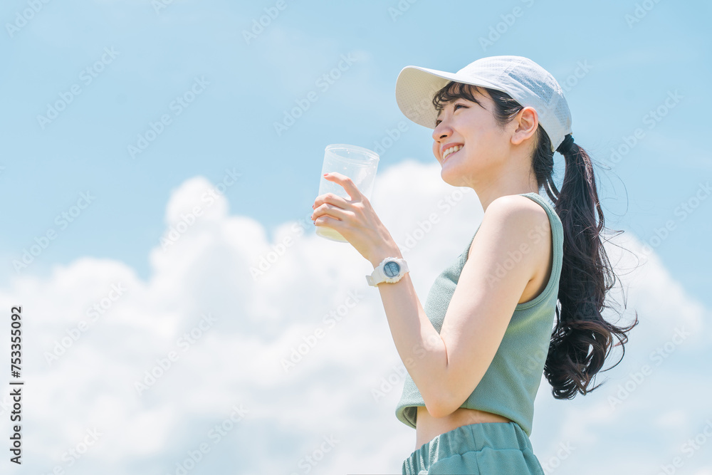 青空の下で運動中にプロテインを飲む若いアジア人女性
