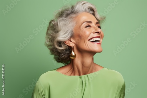 Portrait of smiling senior woman with grey hair on green background.