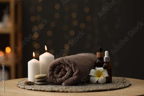 Spa composition. Rolled towel, cosmetic products, stones, burning candles and plumeria flower on table indoors. Space for text