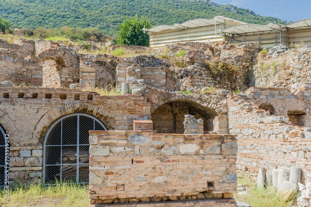 The remnants of brick arches at an archaeological site with a protective shelter overhead, in Ephesus, Turkiye