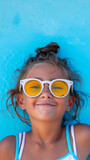 Happy Young Girl in Sunglasses Lying on Blue Background