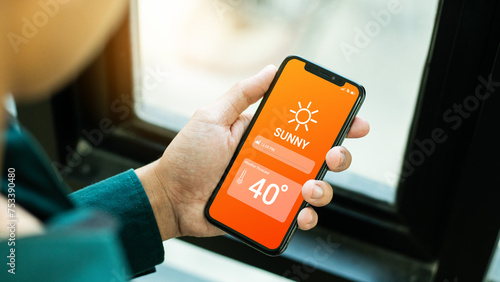 Hand holding smartphone with weather hot sunny day on screen and sunrise on midday at dry forest background. High Temperature Weather show on Mobile Screen on Hot Sunny Day. concept global warming photo