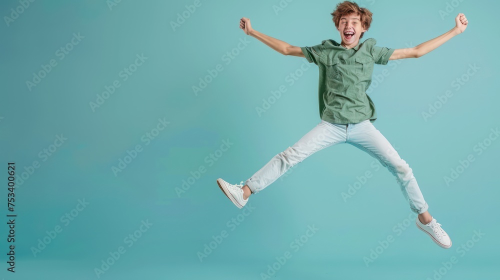 Full body portrait of happy excited young funny teenage boy wearing green shirt, white jeans and sneakers having fun isolated on a blue studio background. Lifestyle and people emotions