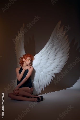 Alluring angel with big wings in black dress sitting on floor