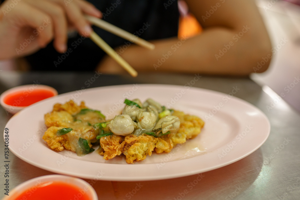 Person eating thai omelette with oyster and greens 