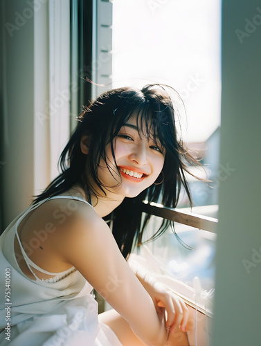 窓辺の自然光を浴びる笑顔のアジア人女性