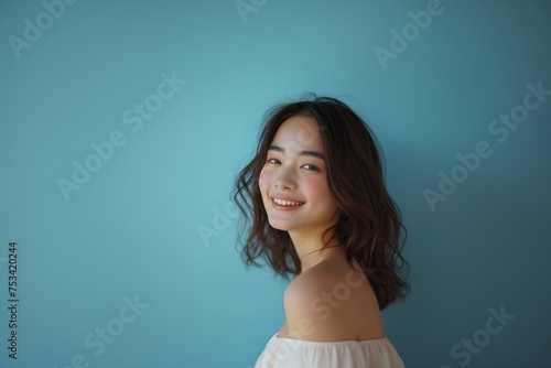 Joyful young woman with a heartfelt smile, dressed in a flowing top, radiates happiness against cool blue backdrop. Lighthearted mirth embodied in a young lady's smile, her casual attire complementing