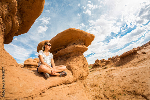 Woman relaxing and meditating on a large and unique sandstone rock while visiting Goblin Valley state park. Woman enjoying a Beautiful desert rock landscape