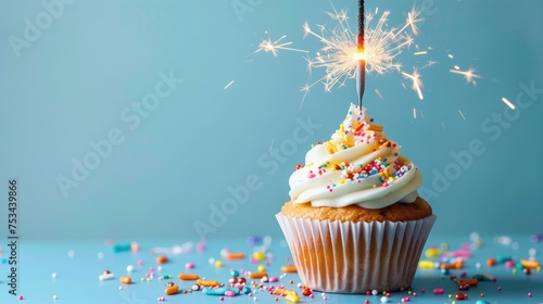 Birthday cupcake with sparkler and sprinkles over a blue background.