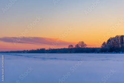 A beautiful winter sunrise scenery of frozen lake and forest. Colorful landscape with dawn skies in Northern Europe. © dachux21