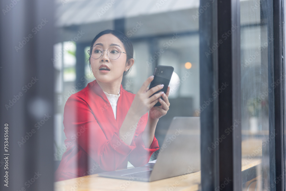 Shot of a young asian woman working using smart phone and notebook computer, woman using smart phone in interior, woman at her workplace using technology, flare light Shot of a young asian woman working using smart phone and notebook computer, woman using smart phone in interior, woman at her workplace using technology, flare light