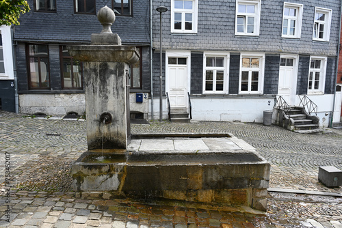Ancient public water tap source on a square in front of slate tile-covered facades of authentic Belgian homes. Source in historical center town of Stavelot, Belgium