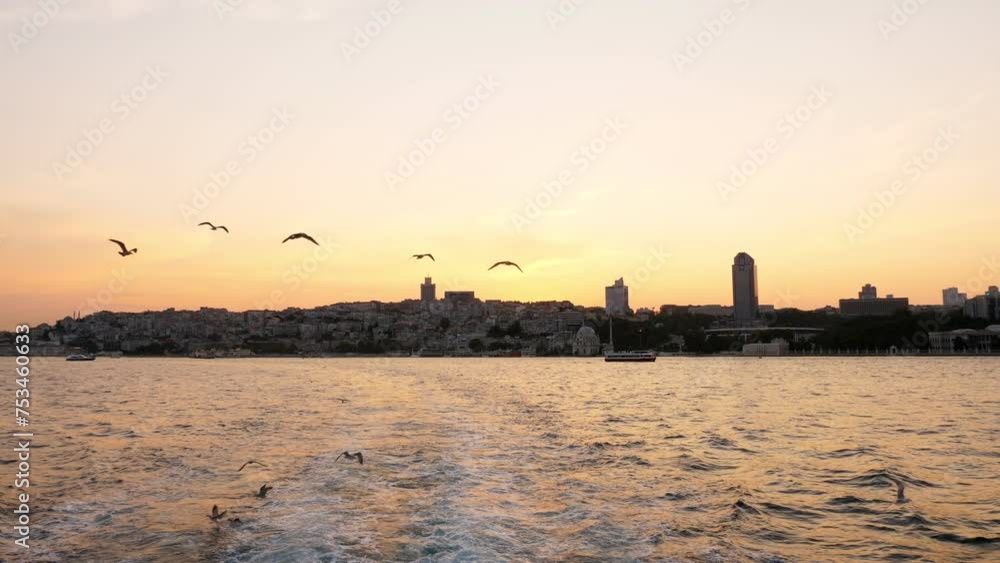 Evening view from ferry sailing through Bosphorus towards Uskudar on European side. City skyline in dusk, small wake on calm water, seagulls soar against serene afterglow sky. Evening view from ferry sailing through Bosphorus towards Uskudar on European side. City skyline in dusk, small wake on calm water, seagulls soar against serene afterglow sky.