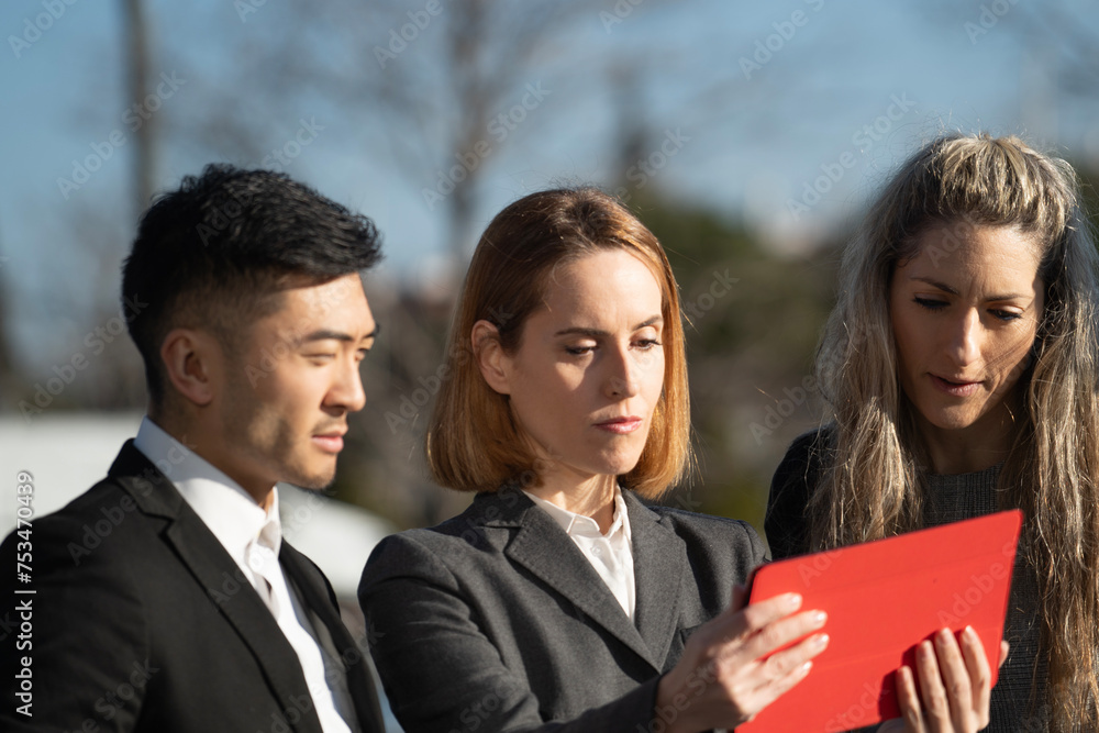 Side view of executive business people discussing about a project with a digital tablet outdoors Side view of executive business people discussing about a project with a digital tablet outdoors