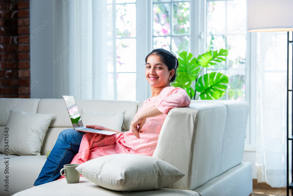 Indian young female with a laptop sitting sofa in a modern living room Indian young female with a laptop sitting sofa in a modern living room