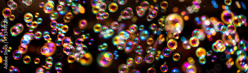 Panorama banner with hundreds of colorful gliding soap bubbles. Fascinating light air filled spheres with an iridescent surface isolated on black background with reflections, partially blurred. 
