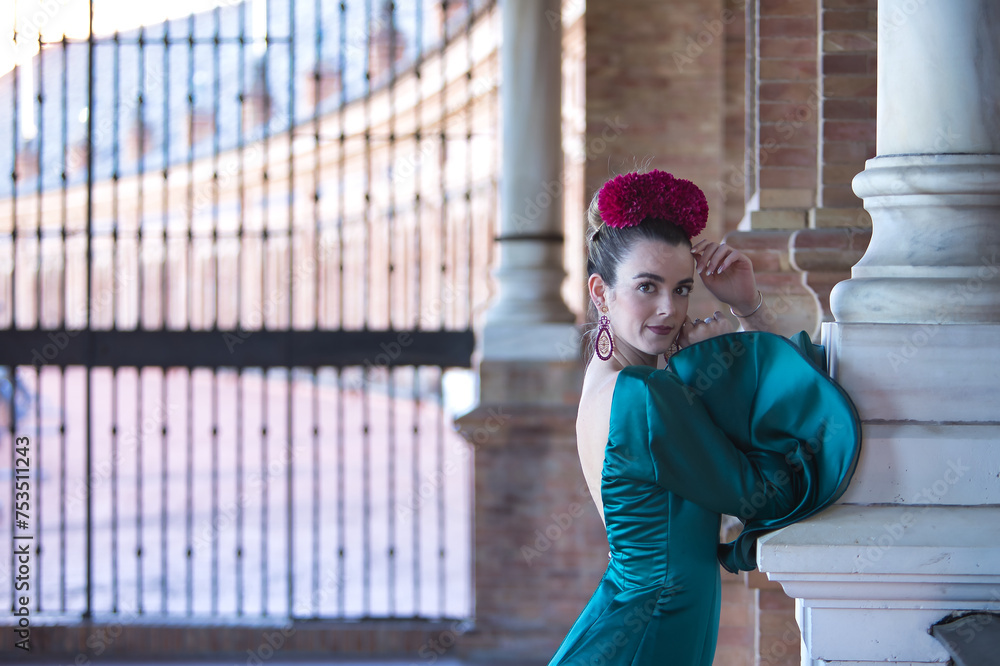 Young, beautiful, blonde woman in typical green colored flamenco suit, posing leaning on a marble column. Flamenco concept, typical Spanish, Seville, Andalusia.