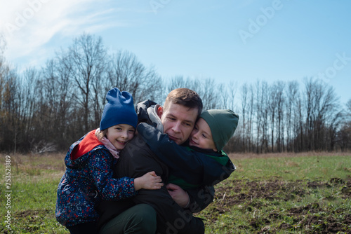 Father and his children, a boy and a girl, spend their leisure time outdoors. Portrait of a happy dad hugging his smiling children. Father and children's day holiday concept
