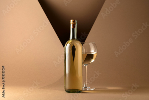 Bottle and glass of white wine on a beige background.