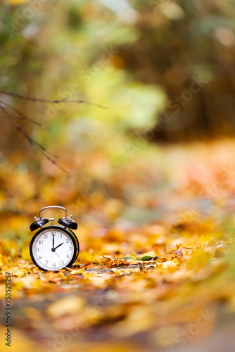 Autumn time or Fall time concept. Vintage Alarm clock black color in the autumn background.