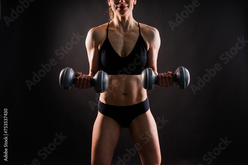 Sporty female doing exercise with dumbbells, silhouette studio shot dark yellow background