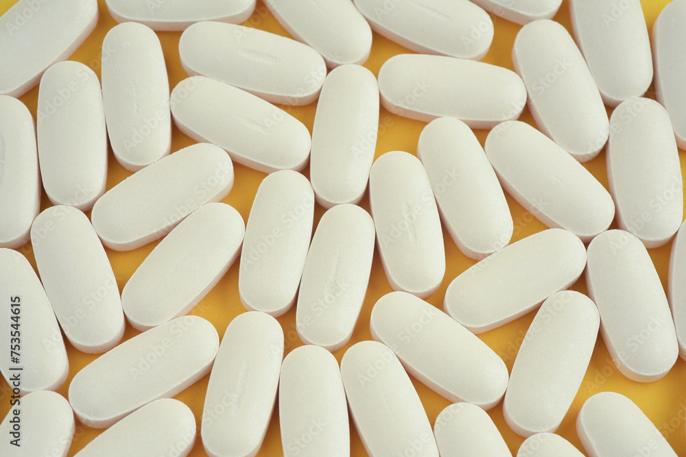 Close up photograph from above of a group of white oval shaped vitamin tablets or pills on yellow background. Top view. Close up photograph from above of a group of white oval shaped vitamin tablets or pills on yellow background. Top view.