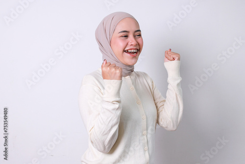 Excited young woman in hijab raising two fist celebrating victory with happy expression