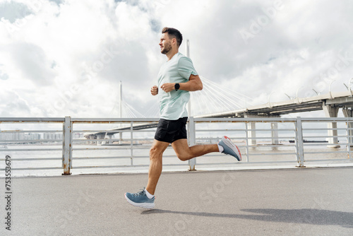 Man jogging on a sunny day with a bridge in the background, focused on his fitness goals. © muse studio