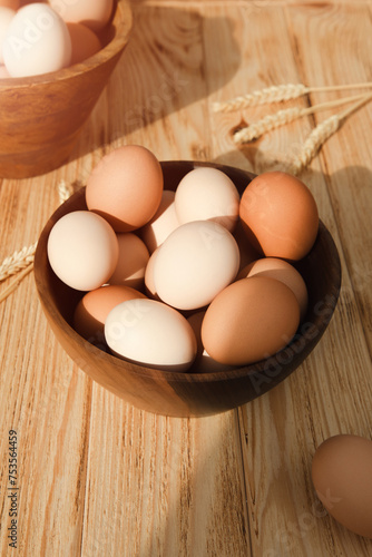 Chicken eggs of different brown and beige shades in a large wooden bowl on a wooden table with beige kitchen towel. Easter background. Top view
