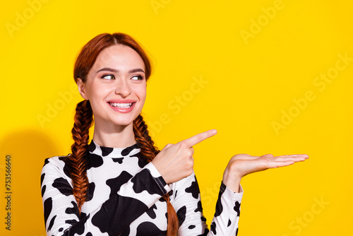 Photo of funky cheerful woman wear cow skin top looking holding arm showing finger empty space isolated yellow color background photo