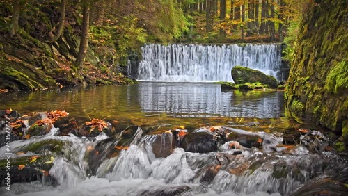 Mountain river with a cascade, cold water flows through the riverbed between wet rocks. Autumn mountain landscape.