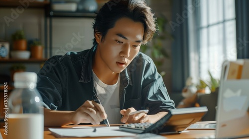 Asian man is using a calculator to calculate his family's monthly miscellaneous expenses at his home.
