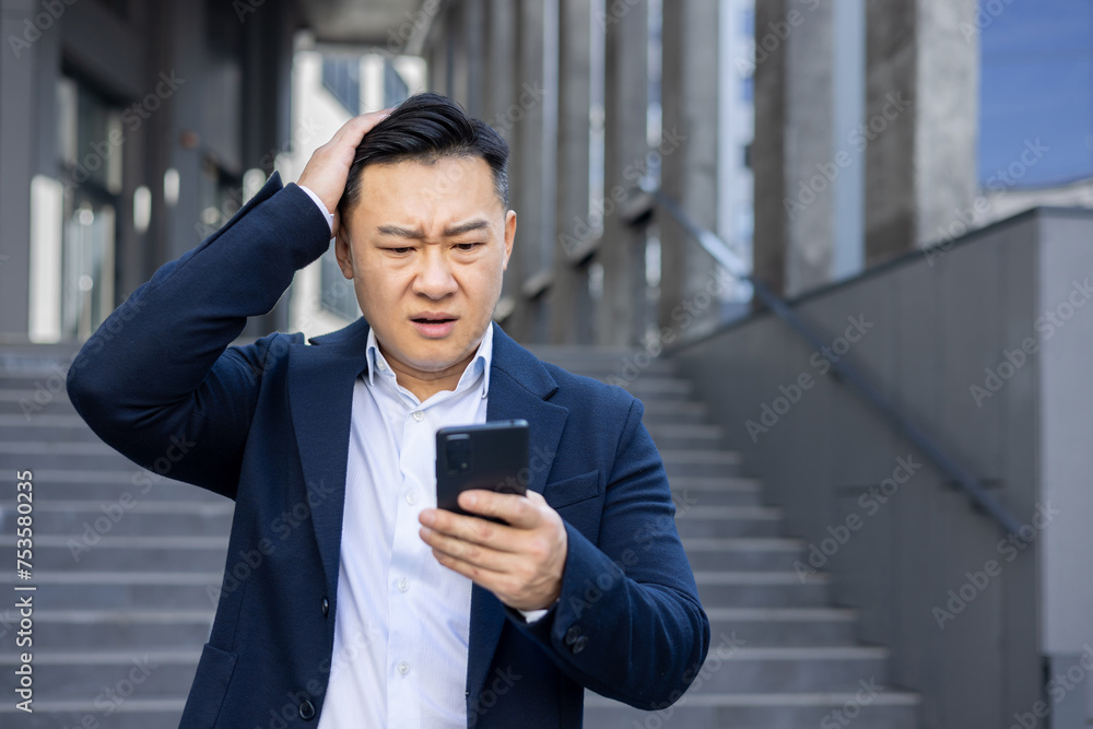 Concerned businessman outdoors looking at smartphone screen with confusion Concerned businessman outdoors looking at smartphone screen with confusion