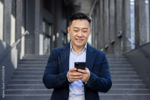 Confident asian businessman texting on smartphone outdoors with urban stairs in the background