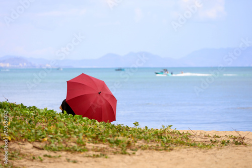 Tourist under red umbrella resting on a sandy sea beach