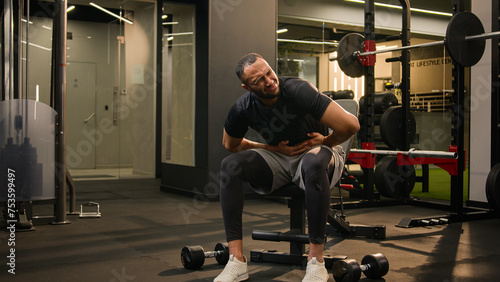 Suffering bad feeling bending African American man sick ill stomach unwell unhealthy belly indigestible poisoning abdominal pain sportsman athlete bodybuilder man in sport gym suffer abs workout ache