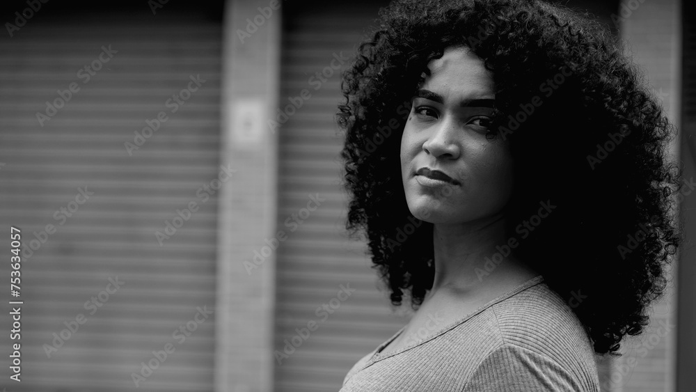 Empowered African American Woman in Urban Setting, Tracking Close-Up of Confident Young Female Face in bold black and white, monochromatic. One black person standing in street staring at camera - obrazy, fototapety, plakaty 