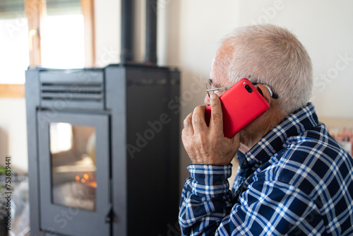 Old man in his eighties talking on his mobile phone, sitting on the sofa next to the pellet cooker. Brown corduroy trousers and blue checked flannel shirt.