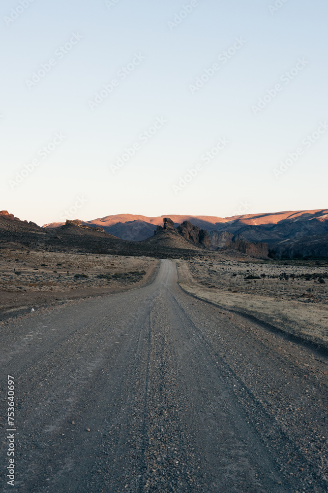 The golden hour casts soft light over a remote dirt road, leading into the vast, rugged terrain of the Argentinian Patagonia during summer The golden hour casts soft light over a remote dirt road, leading into the vast, rugged terrain of the Argentinian Patagonia during summer