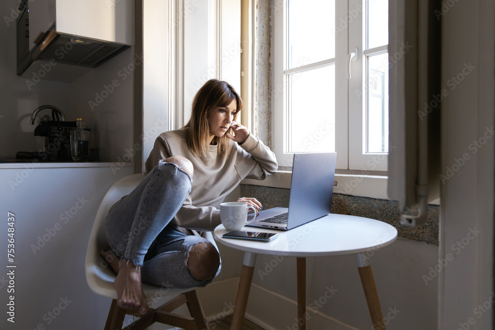 Thoughtful woman working from home near window Thoughtful woman working from home near window