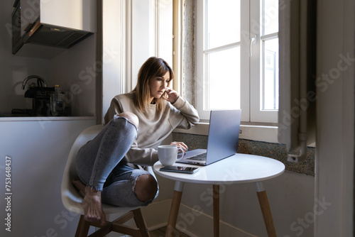 Thoughtful woman working from home near window photo
