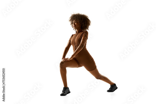 Fitness instructor demonstrating lunge training in brown activewear against white studio white background. Exercises for legs. Concept of sport, mourning routine, active and healthy lifestyle, action.