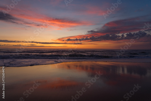 Sunset landscape of a beautiful and paradisaical beach with the clouds reflected on the water. Summer and vacations concept background. photo