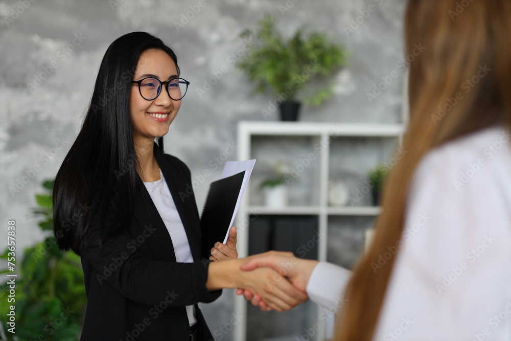 In a professional office, an Asian businesswoman seals successful deals through confident handshakes and teamwork.